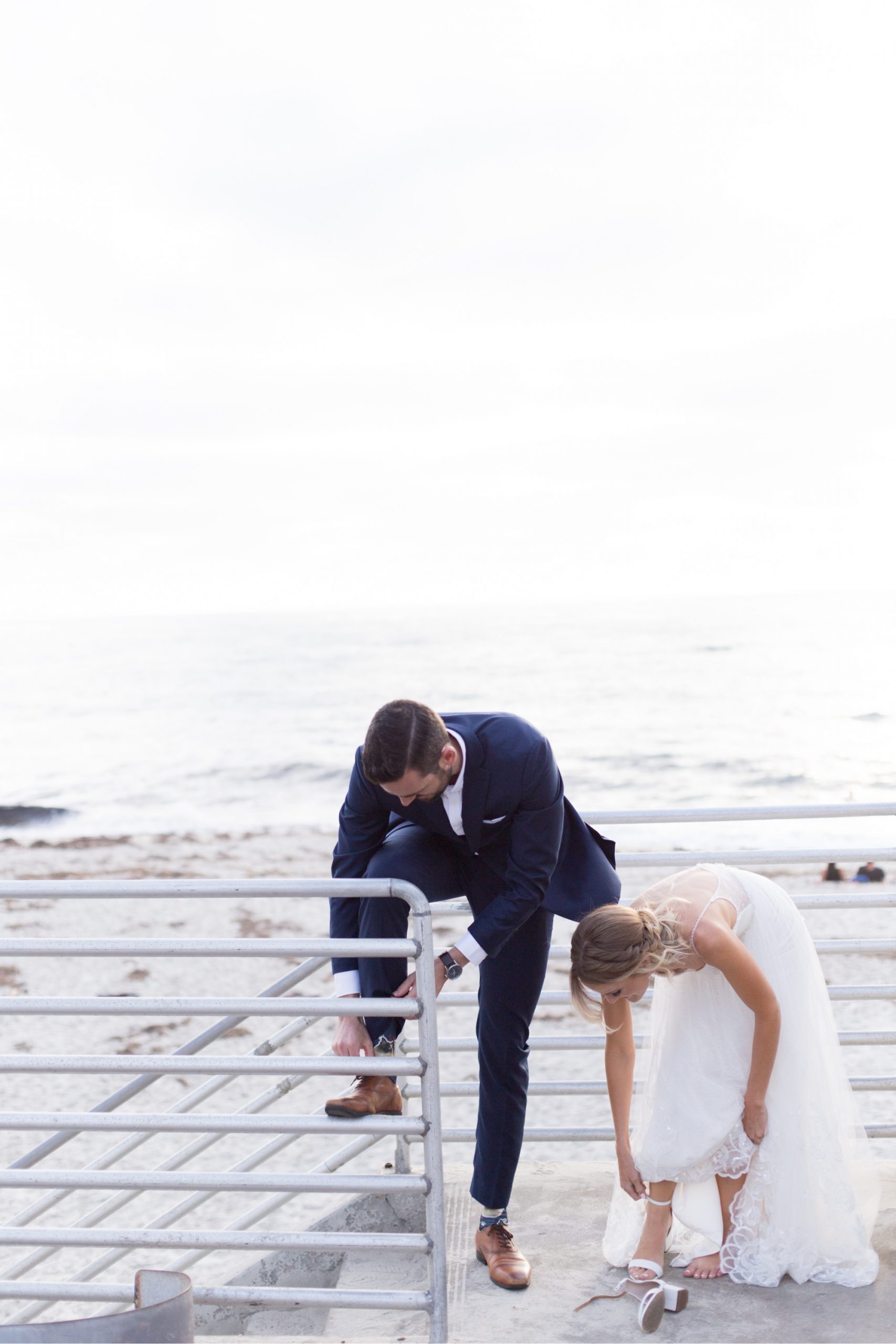 bride and groom taking their shoes off at beach