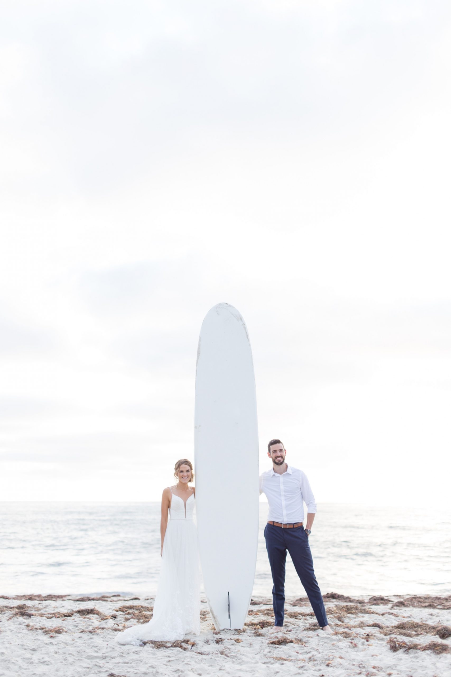 bride and groom standing with surfboard at la jolla wedding