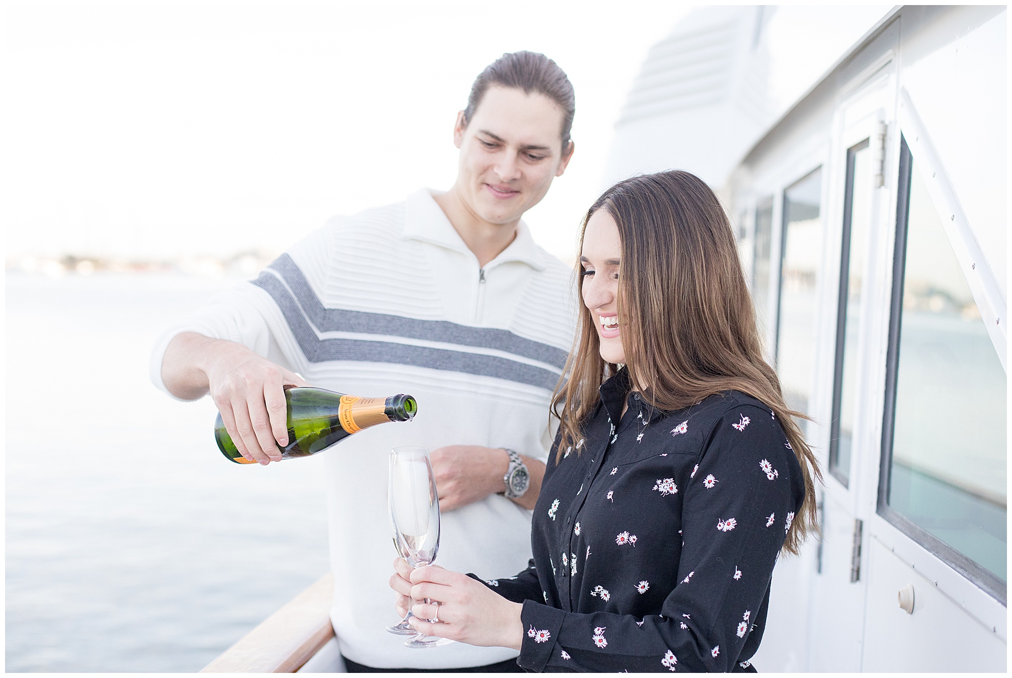 engaged couple popping champagne on boat