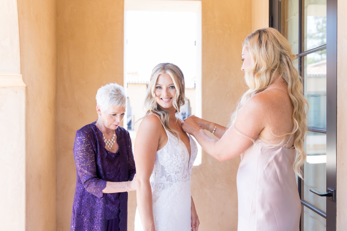 bride putting on her wedding dress with her mom and sister