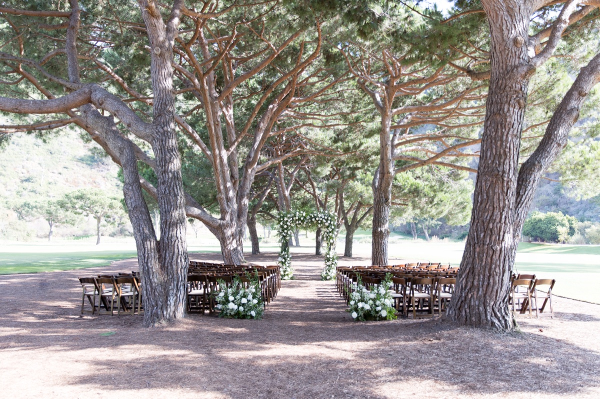 Outdoor wedding ceremony setup at ranch at laguna beach with white floral arch and tall trees in Laguna Beach