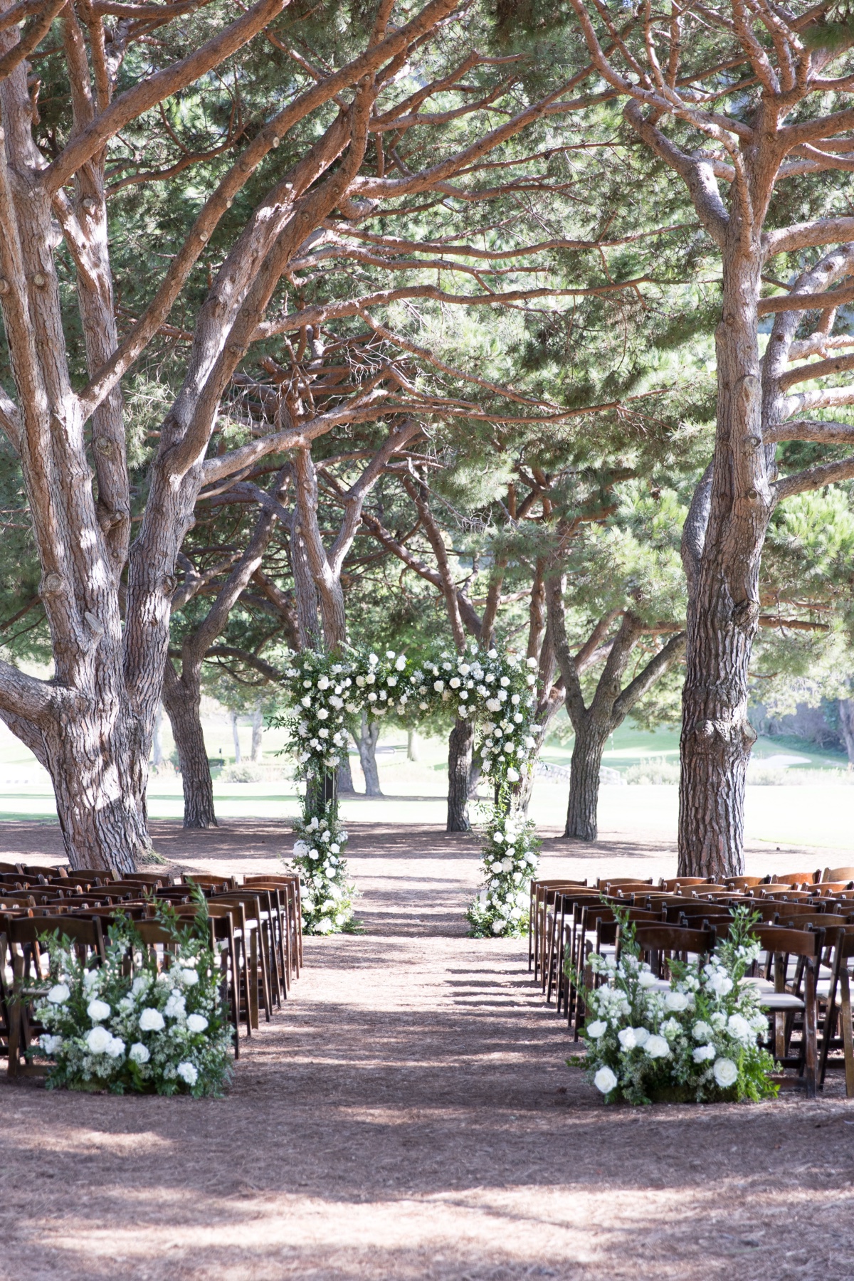 Outdoor wedding ceremony setup at ranch at laguna beach with white floral arch and tall trees in Laguna Beach