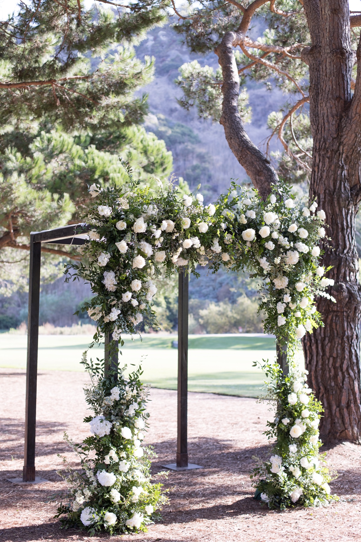 Outdoor wedding ceremony setup at ranch at laguna beach with white floral arch and tall trees in Laguna Beach