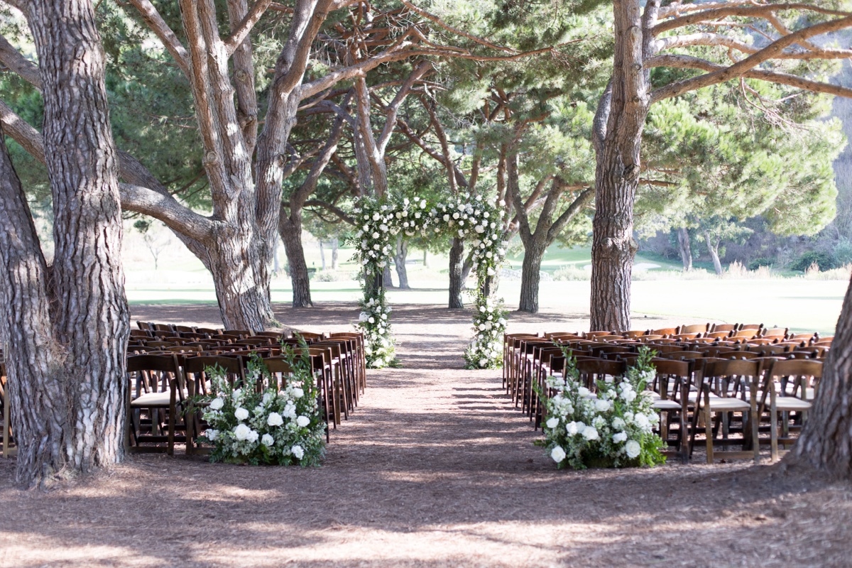 Outdoor wedding ceremony setup at ranch at laguna beach with white floral arch and tall trees in Laguna Beach