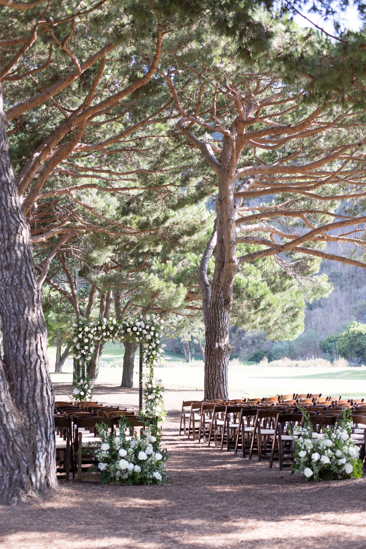 Outdoor wedding ceremony setup at ranch at laguna beach with white floral arch and tall trees in Laguna Beach