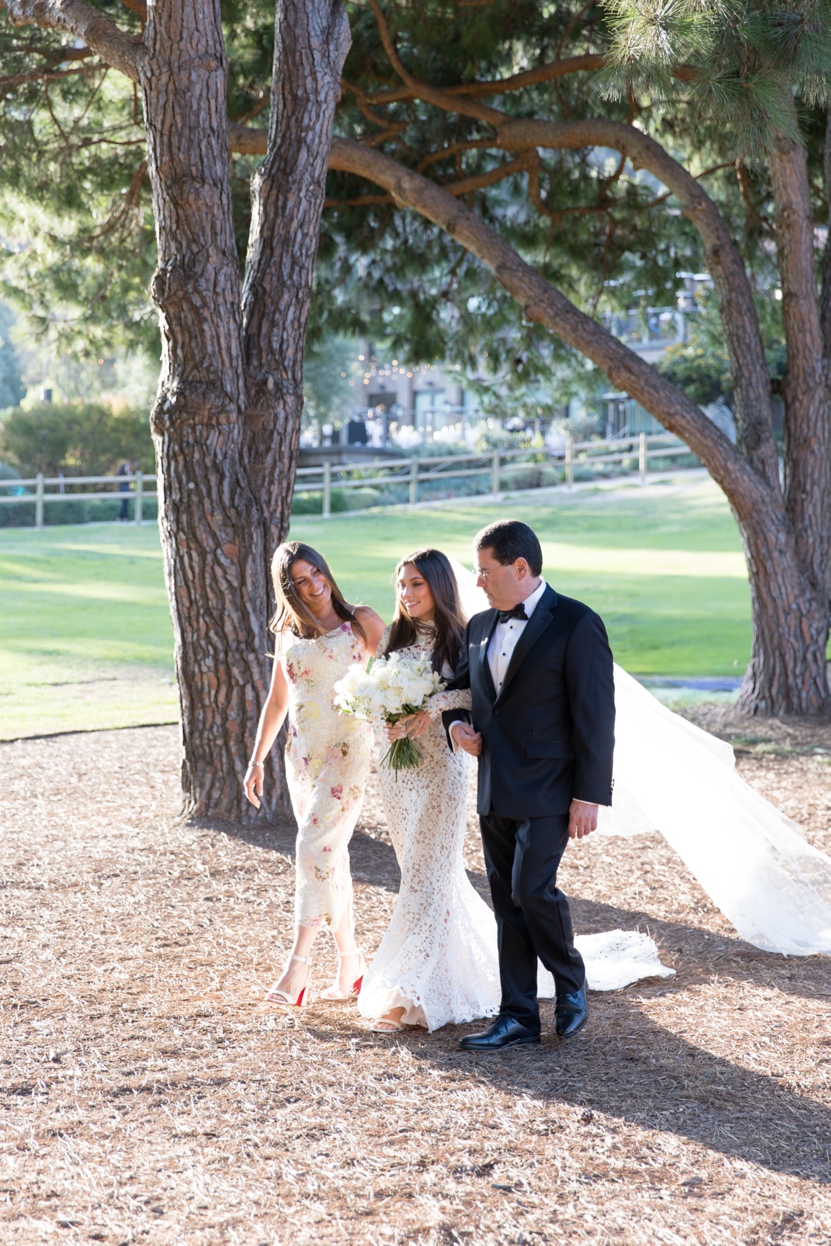Outdoor wedding ceremony beneath tall trees at ranch at laguna beach with white floral arch and elegant details