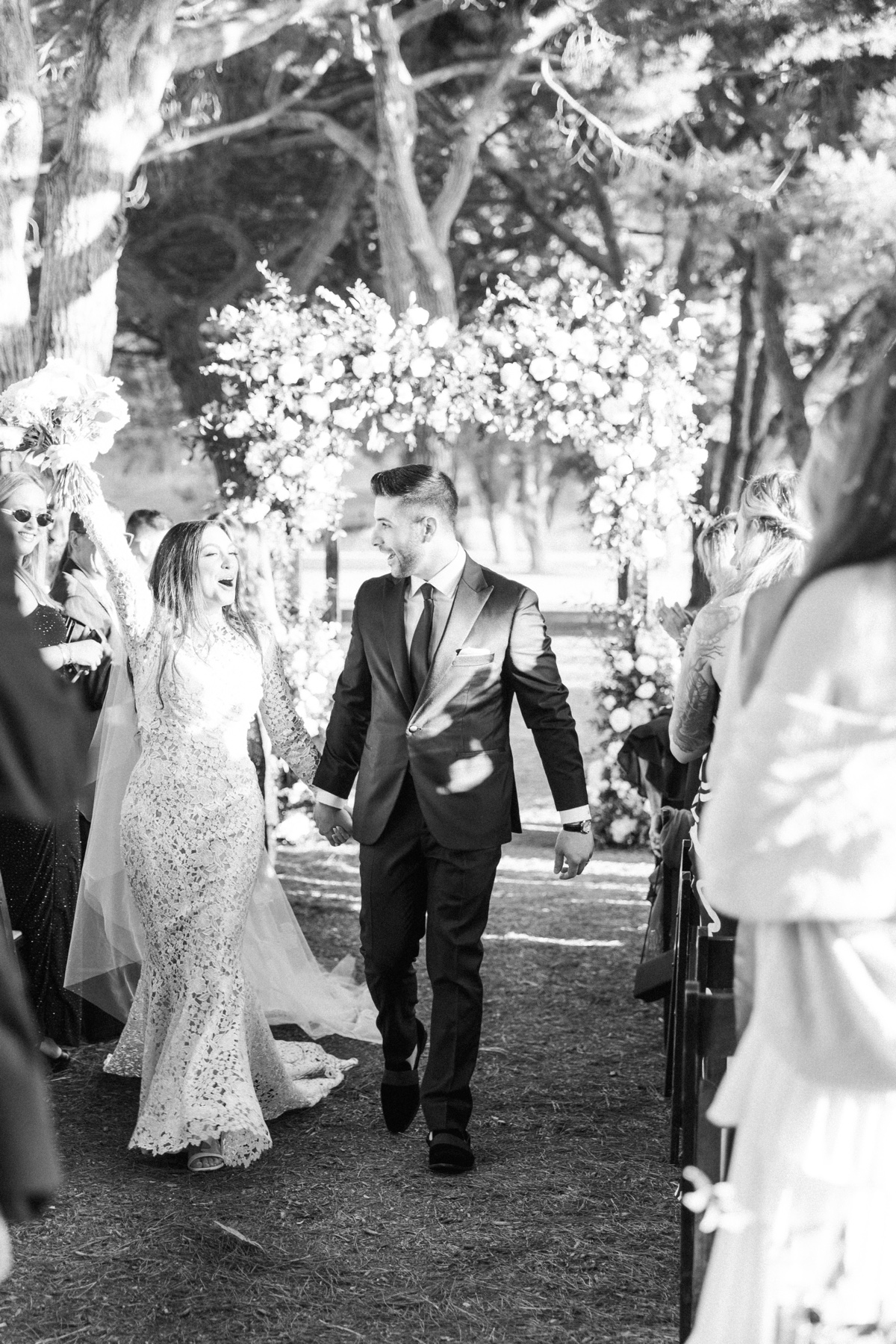 Outdoor wedding ceremony beneath tall trees at ranch at laguna beach with white floral arch and elegant details
