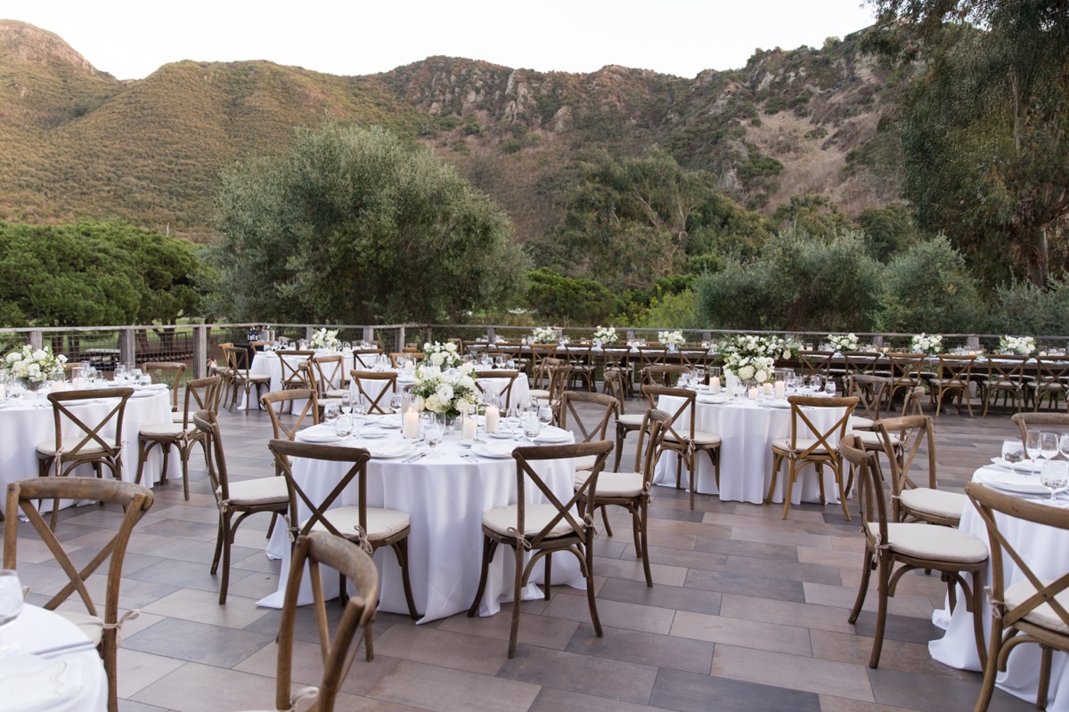 Elegant outdoor wedding reception at Laguna Ranch featuring white floral centerpieces, candles, and wooden chairs