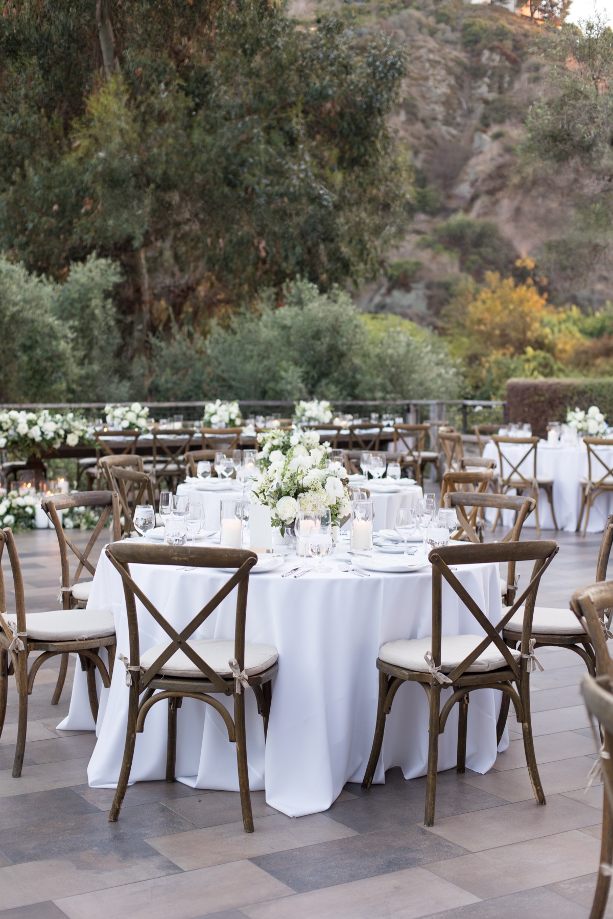 Elegant outdoor wedding reception at The Ranch at Laguna Beach featuring white floral centerpieces, candles, and wooden chairs