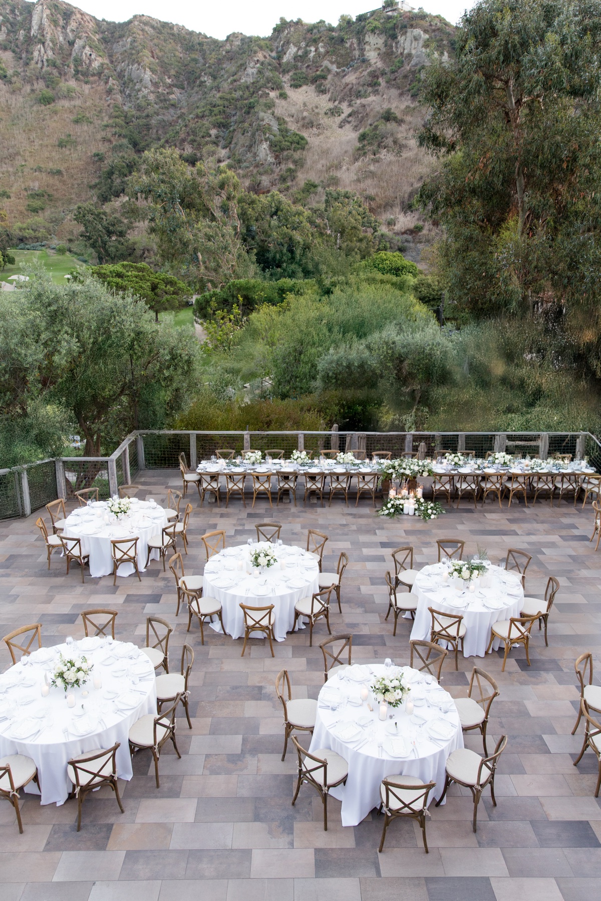 Elegant outdoor wedding reception at The Ranch at Laguna Beach featuring white floral centerpieces, candles, and wooden chairs
