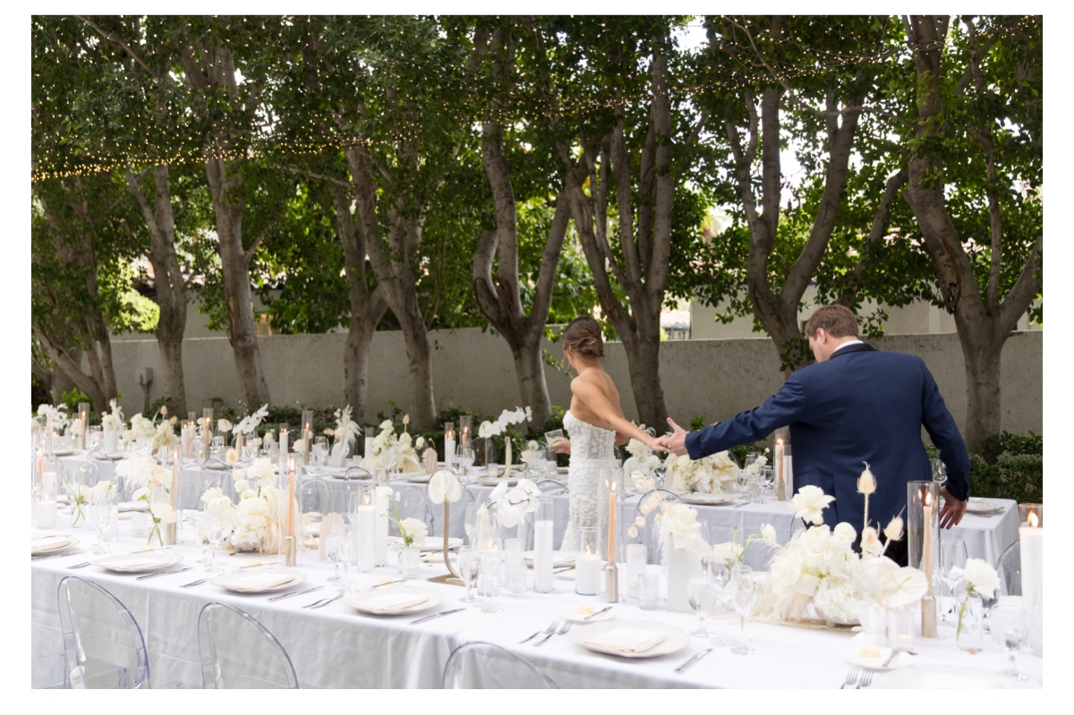 bride and groom walking through their wedding reception that was filled with white and champagne florals.